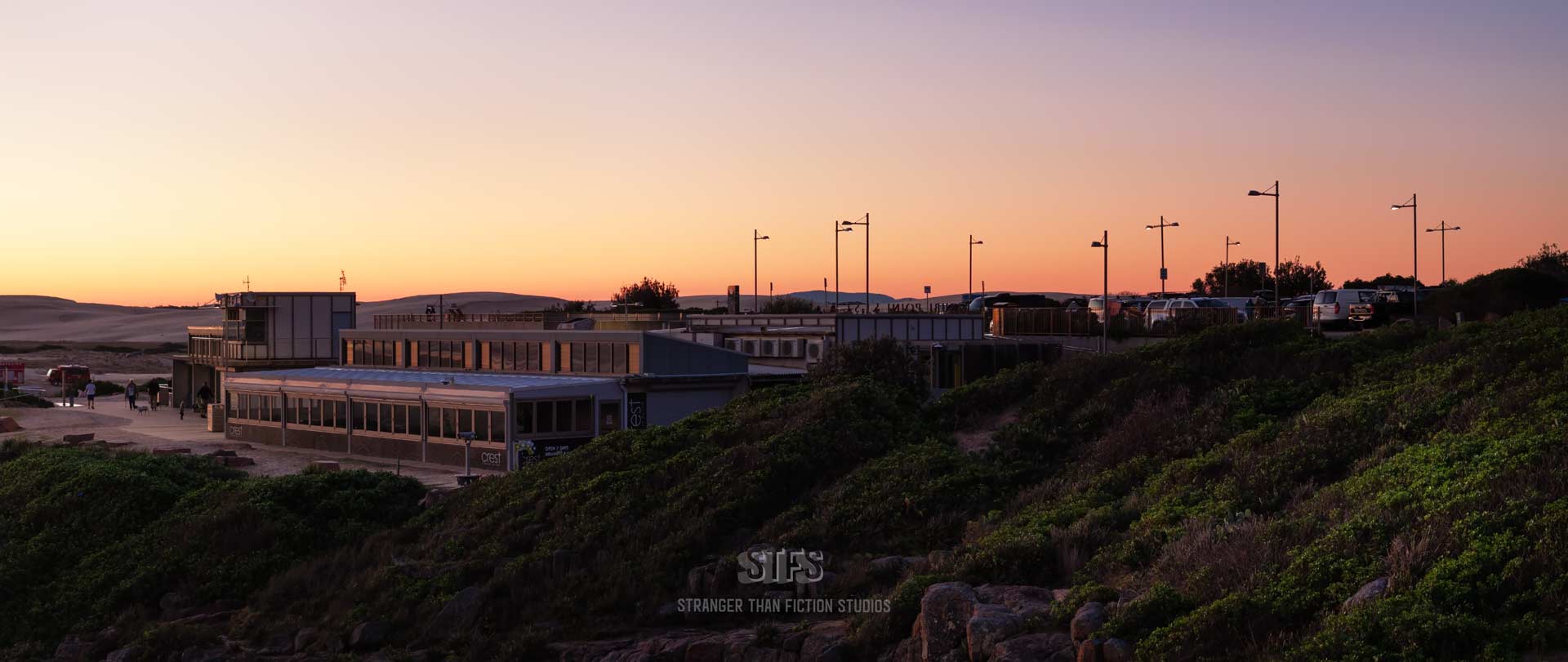 Panoramic Drone Image Of The Birubi Point Surf Club And Crest Cafe At Birubi Beach in Port Stephens. Image Captured At Sunset With Golden Sky Above And Sand Dunes Behind.